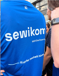 Nahaufnahme eines blauen Laufshirts mit dem weißen Aufdruck „sewikom“ und dem Hashtag „#MitGlasfaserinsZiel“.